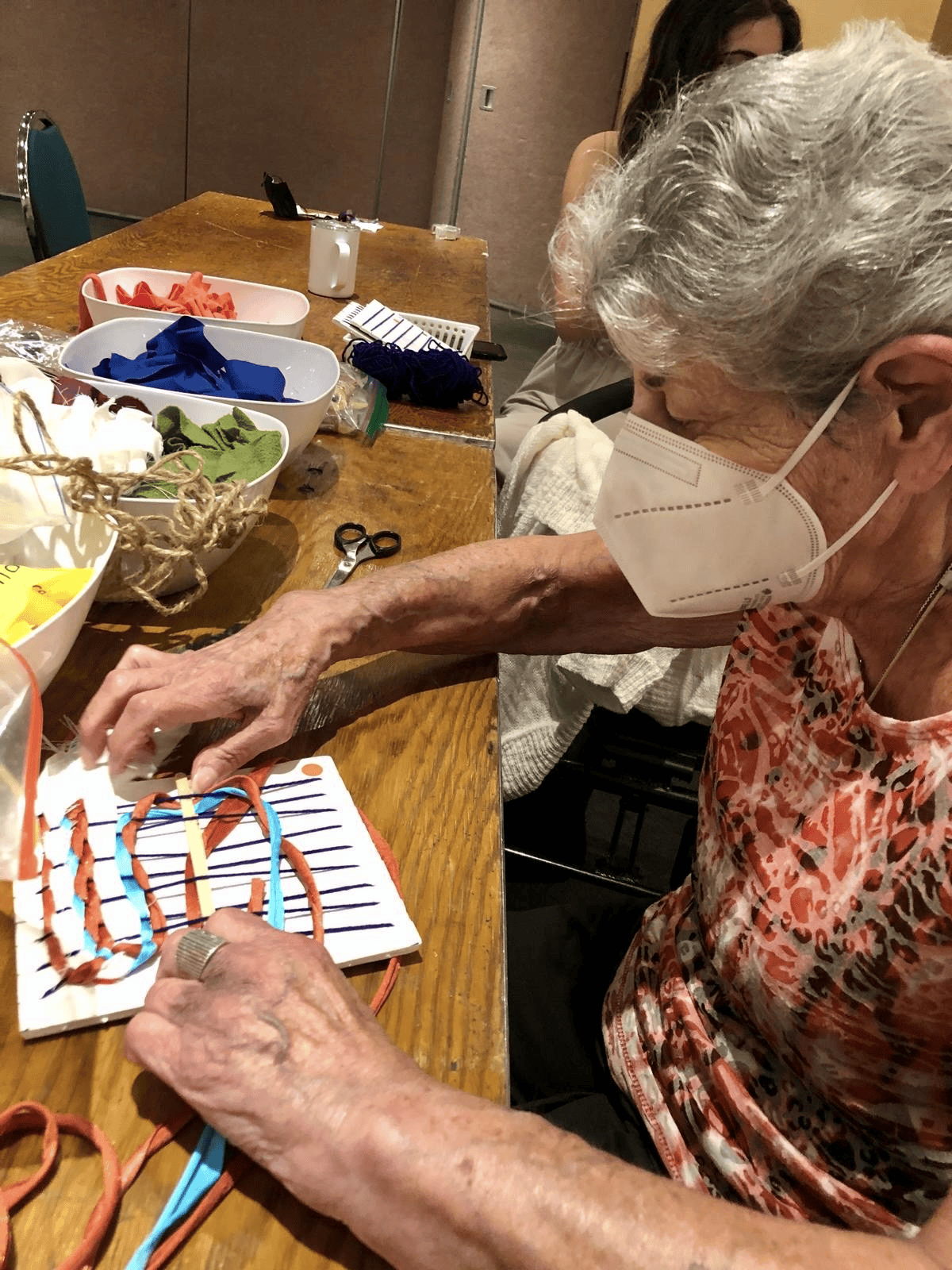 Older adult weaving with colourful fabric strips on a loom